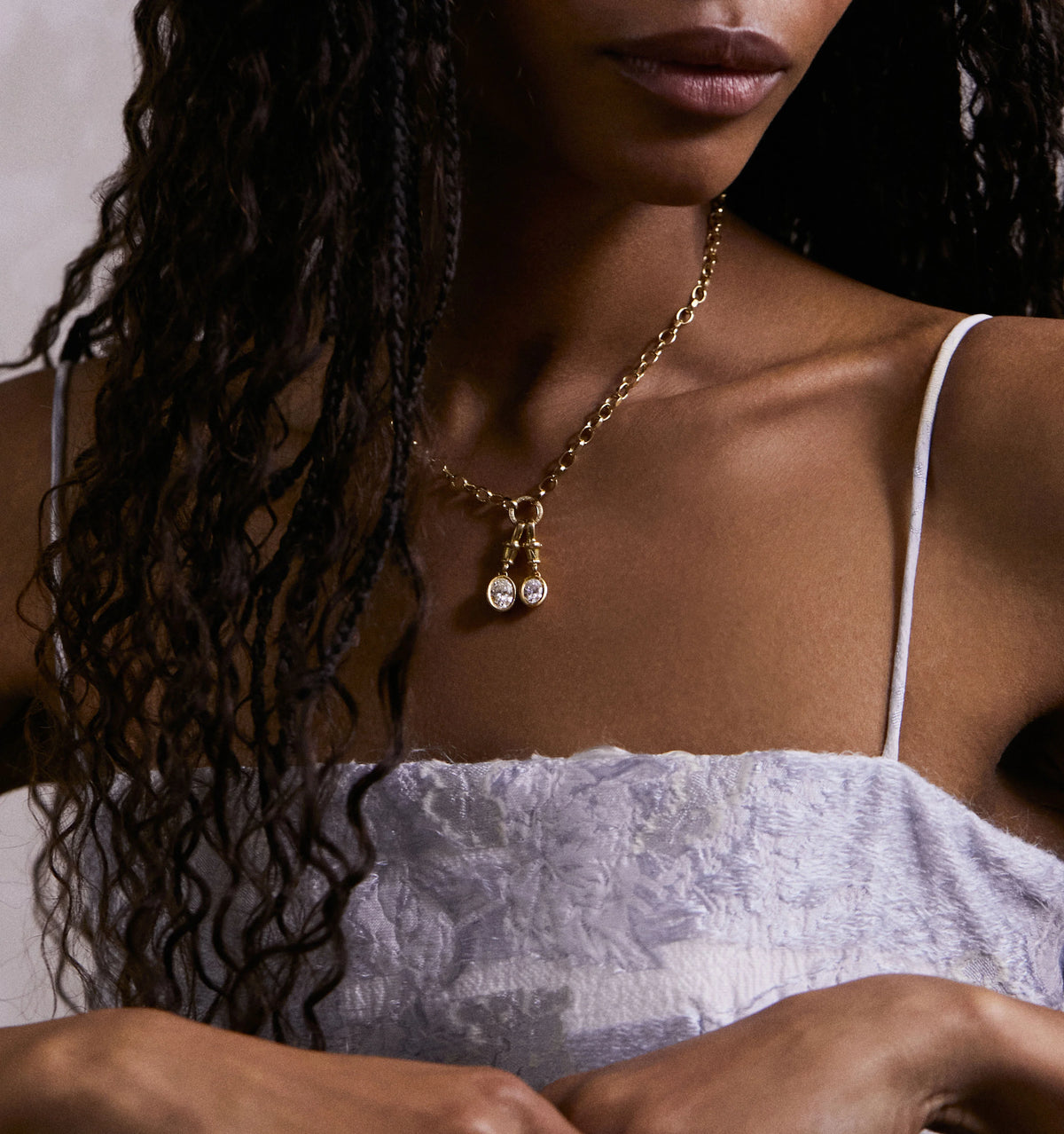 Woman wearing a gold chain necklace featuring two oval pendants with diamonds.