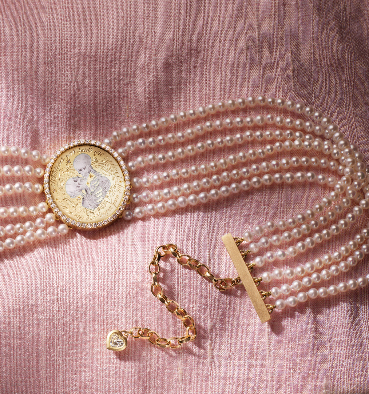 Gold bracelet featuring a circular charm with a portrait, adorned with multiple strands of pearls on a pink fabric background.