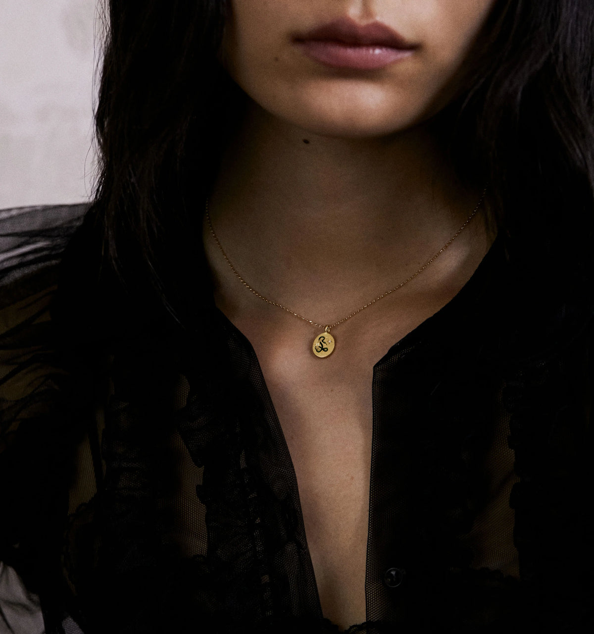 Woman wearing a gold necklace with a round pendant featuring an engraved design.