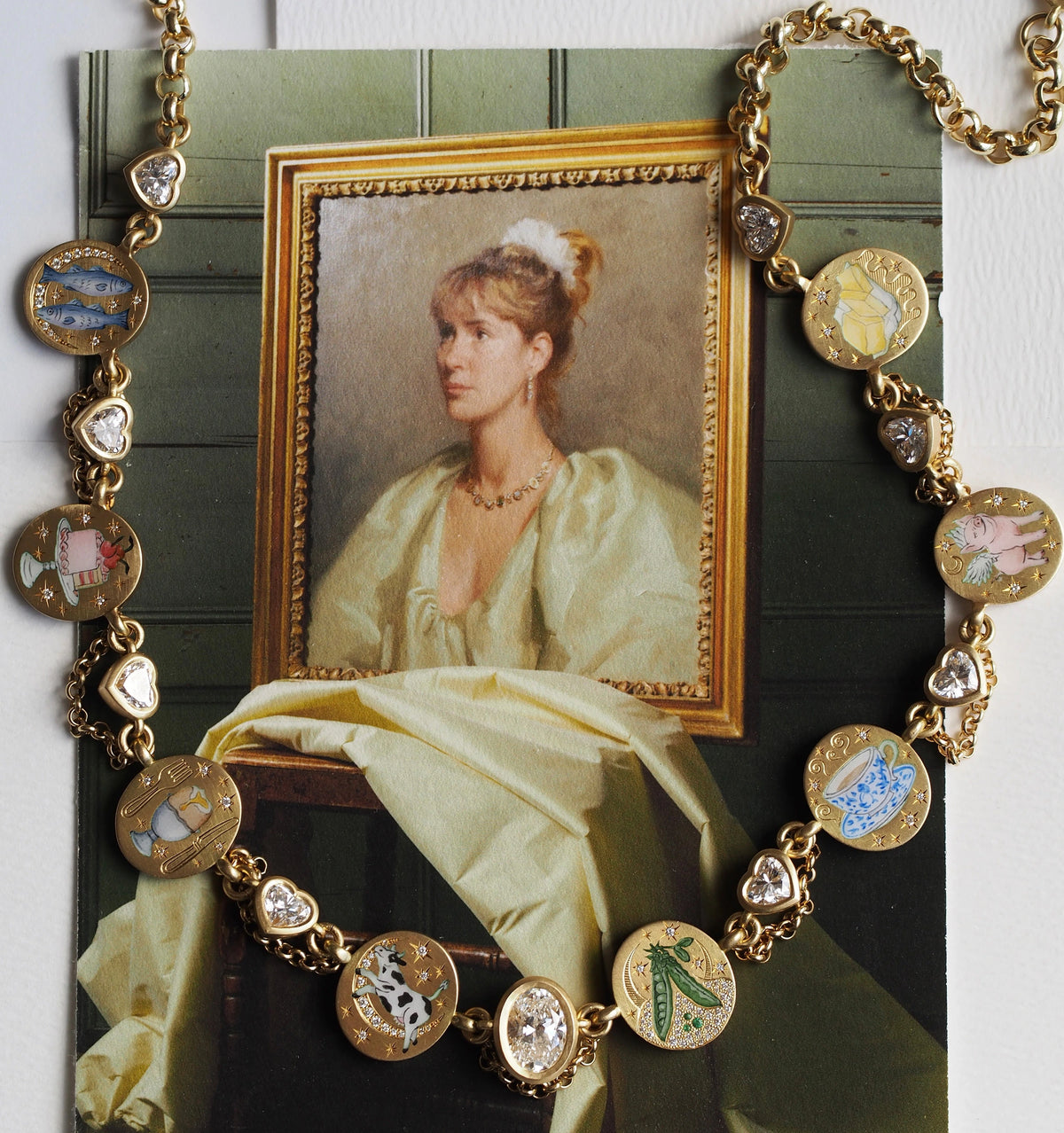 Gold necklace with enamel charms of fish, a cow, a pig, peas, and a teacup, set with diamonds, over a vintage portrait.