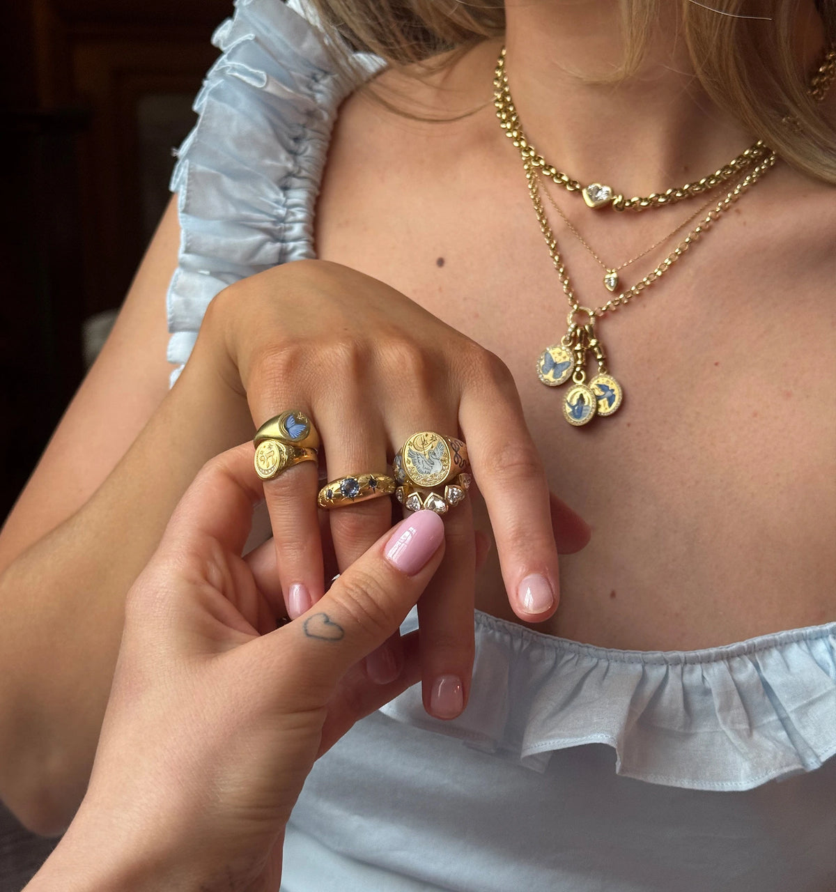 Woman wearing multiple gold rings with blue enamel and a gold necklace featuring gold pendants.