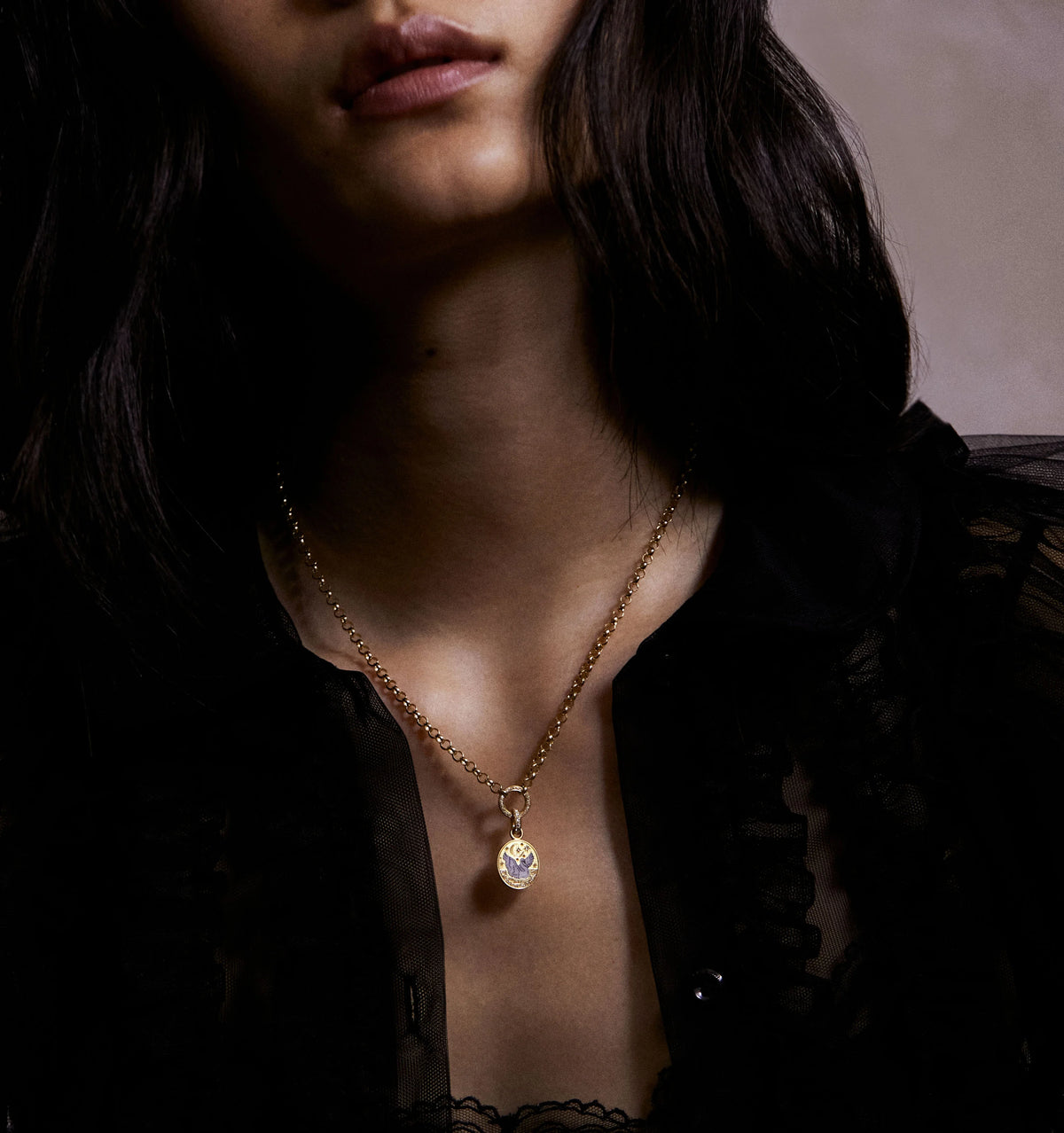Woman wearing a gold necklace with an engraved pendant featuring a floral design, against a dark background.