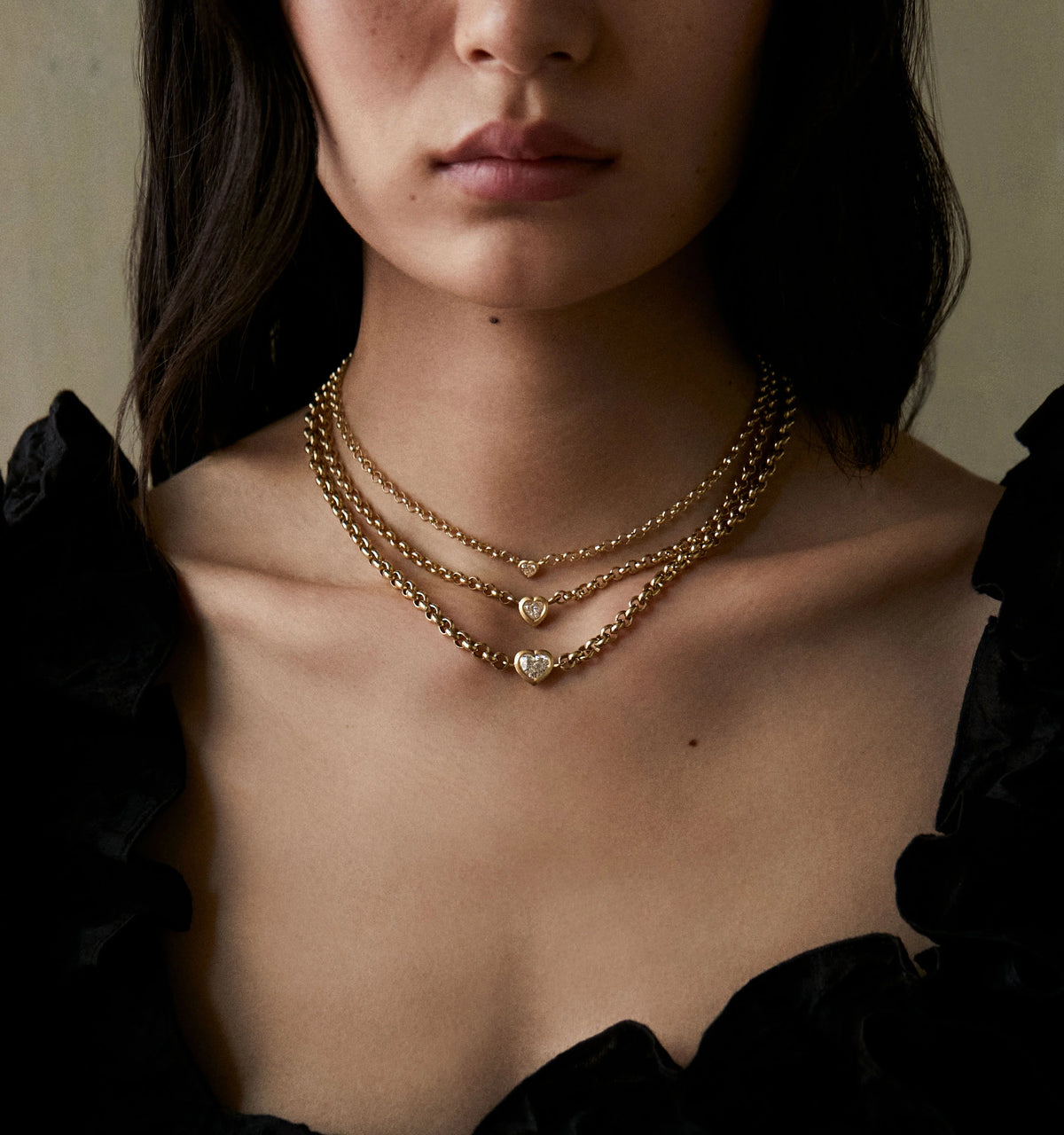 Woman wearing three layered gold chain necklaces, each featuring a heart-shaped pendant with diamonds.