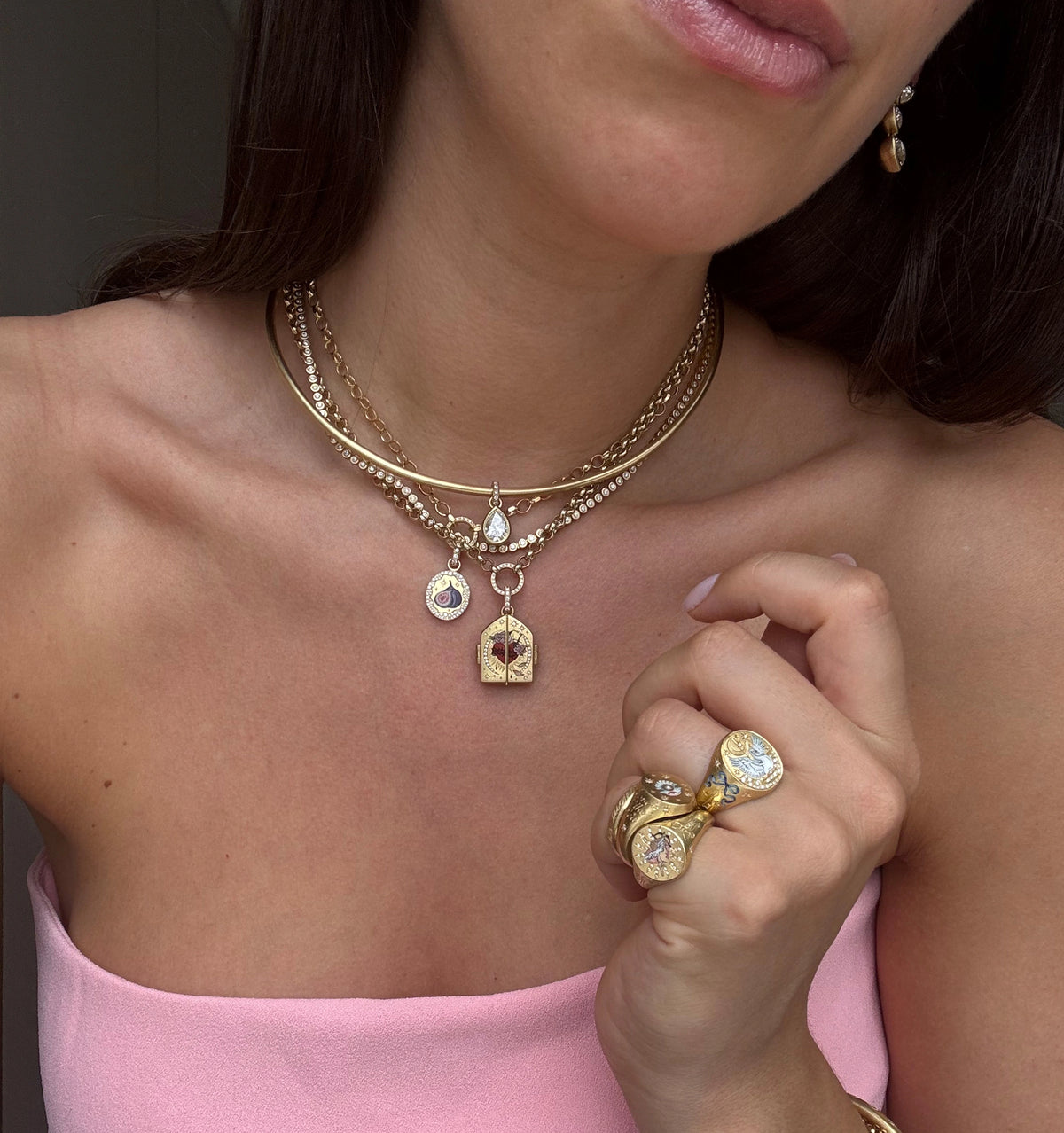 Woman wearing layered gold necklaces with charms, rings featuring multiple diamonds, and gold hoop earrings.
