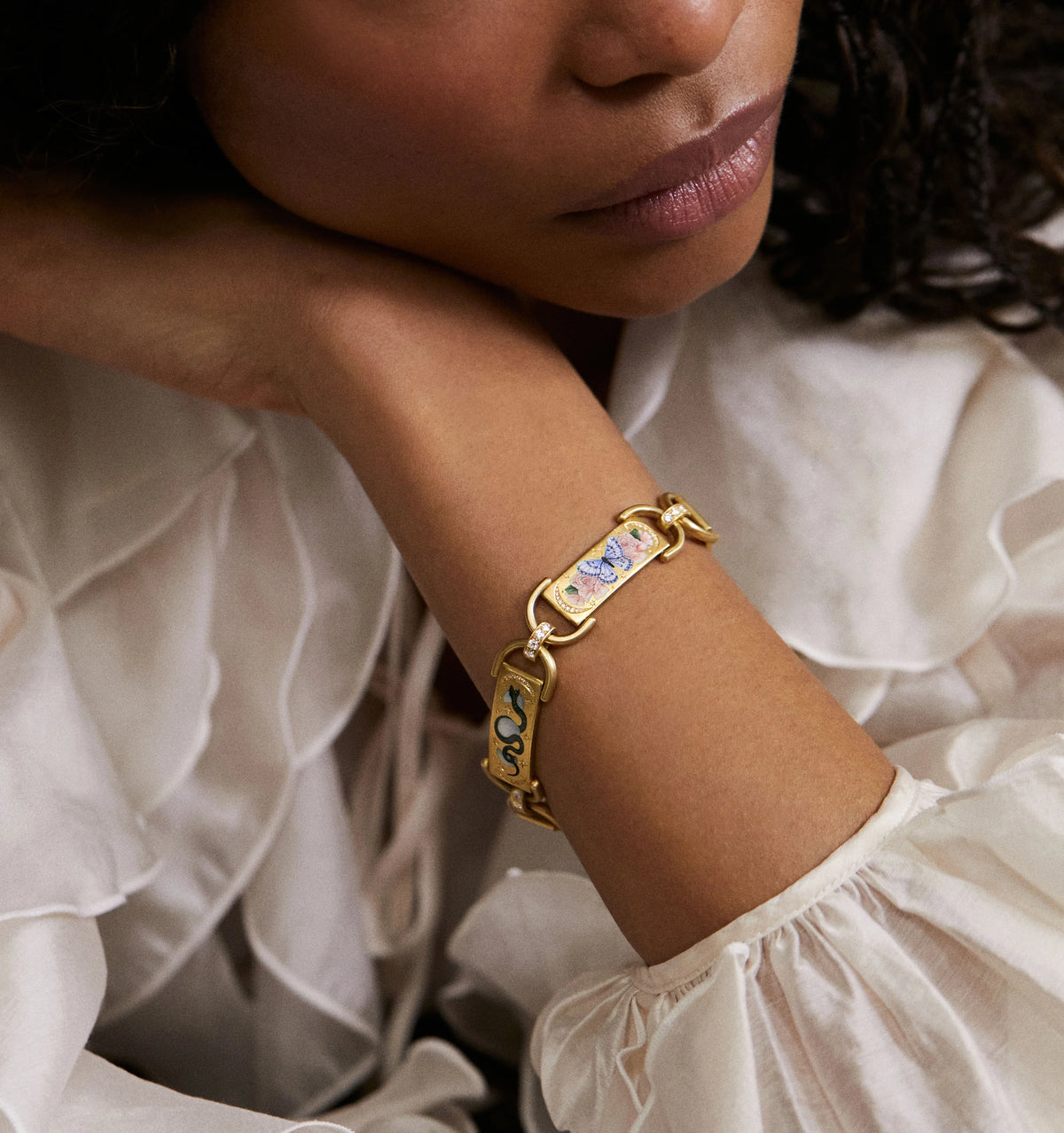Woman wearing a gold bracelet featuring floral enamel designs and a decorative clasp.