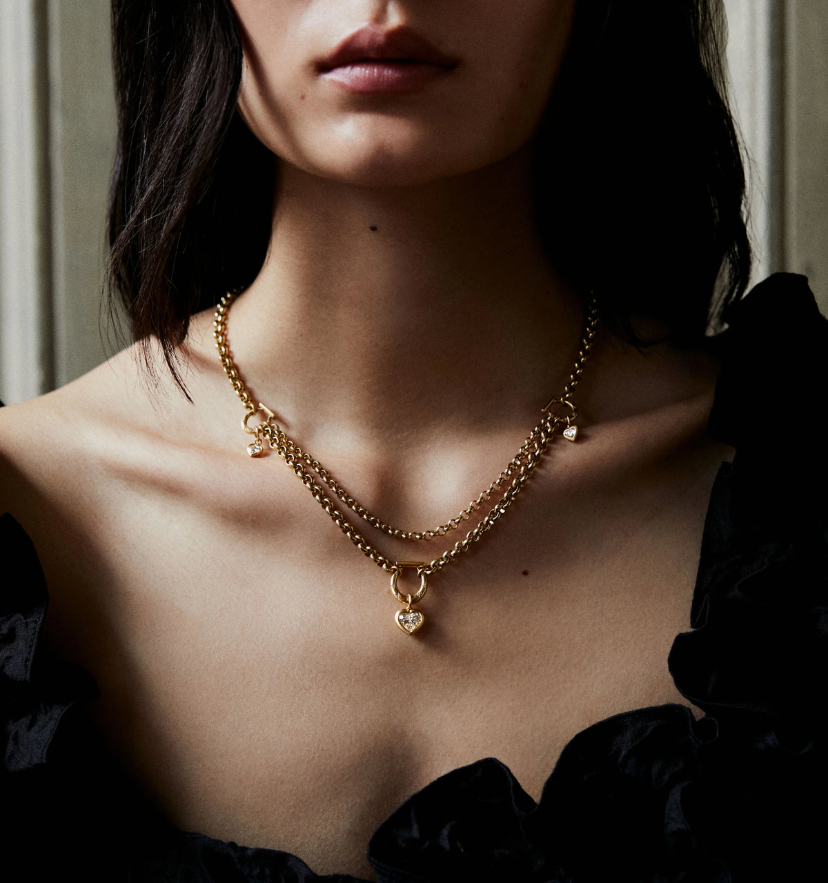 Woman wearing a gold layered chain necklace with a heart pendant and a small charm.