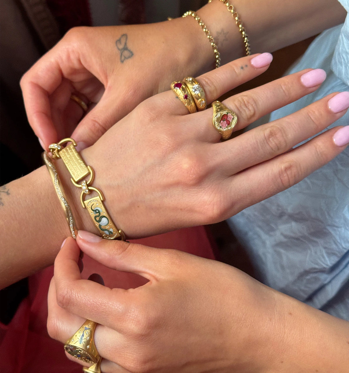 Woman fastening a gold bracelet with a snake design in enamel on another hand wearing rings with rubies, diamonds, and florals.