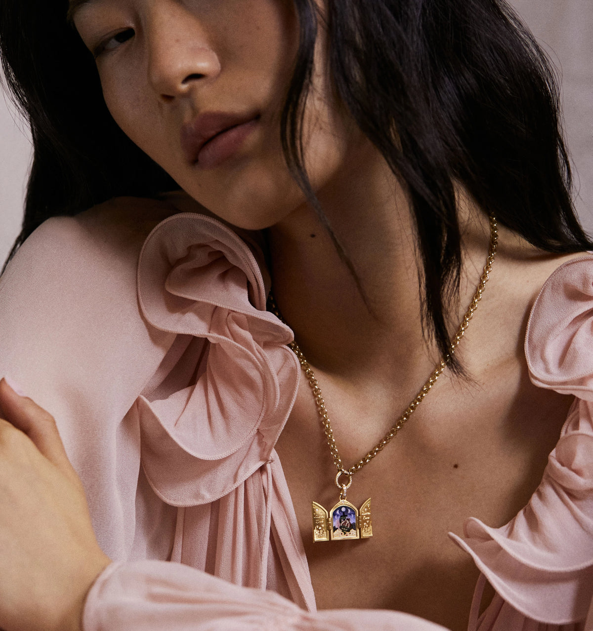Woman wearing a gold necklace with an ornate pendant featuring a purple enamel design.