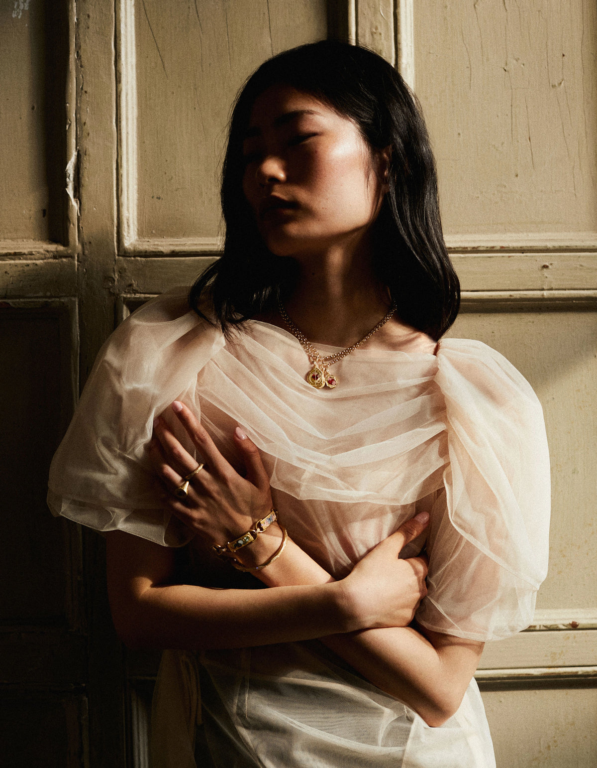 Woman wearing gold jewellery, including a necklace with rubies, gold rings, and a bracelet, set against a neutral background.