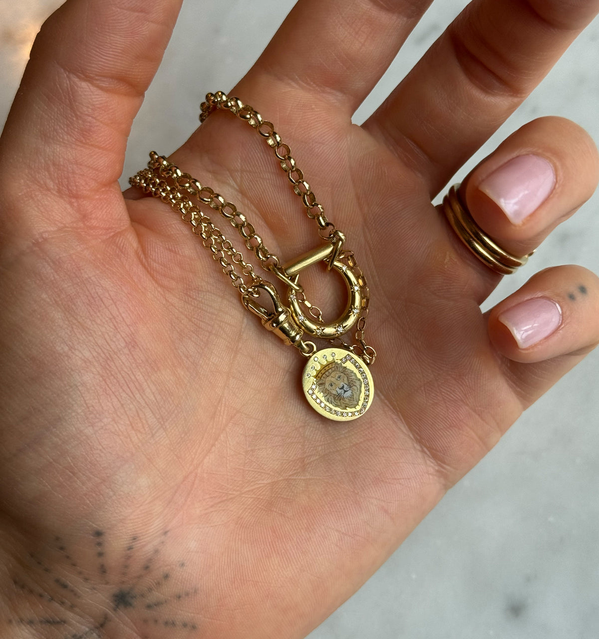 Woman wearing a gold necklace with a lion pendant and multiple chains, holding it in her hand.