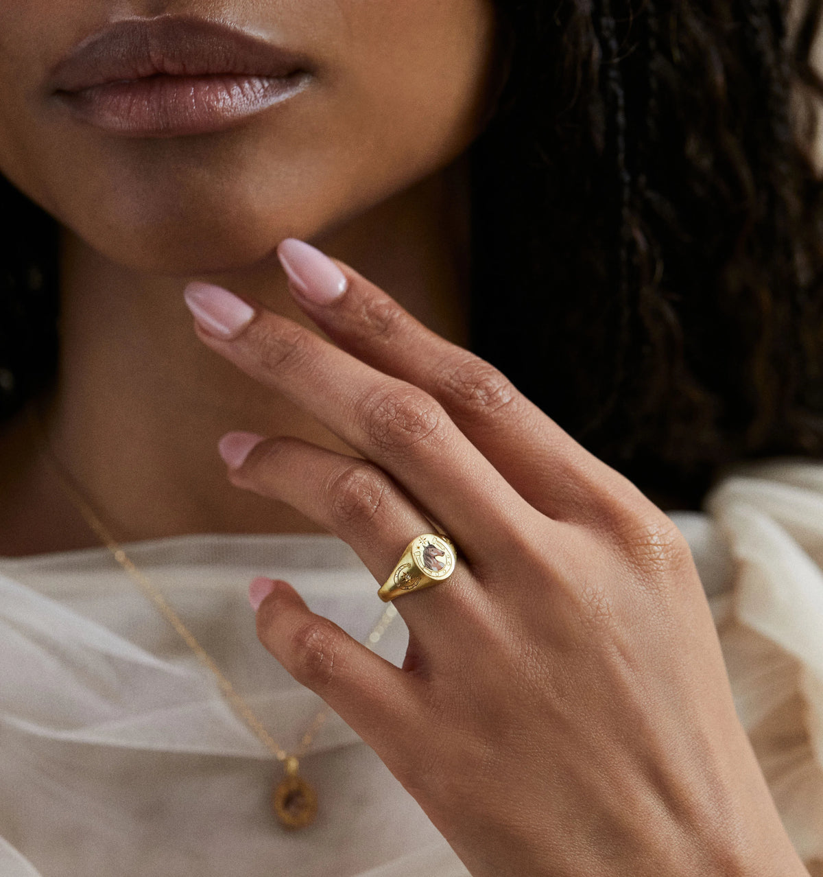 Woman wearing a gold ring featuring a rose motif and gold necklace with a pendant.