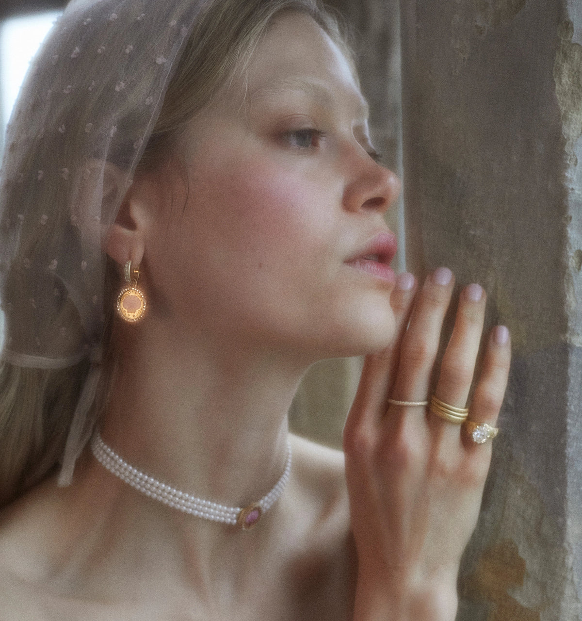 Woman wearing gold earrings, a pearl choker, a gold ring with a diamond, and gold bands.
