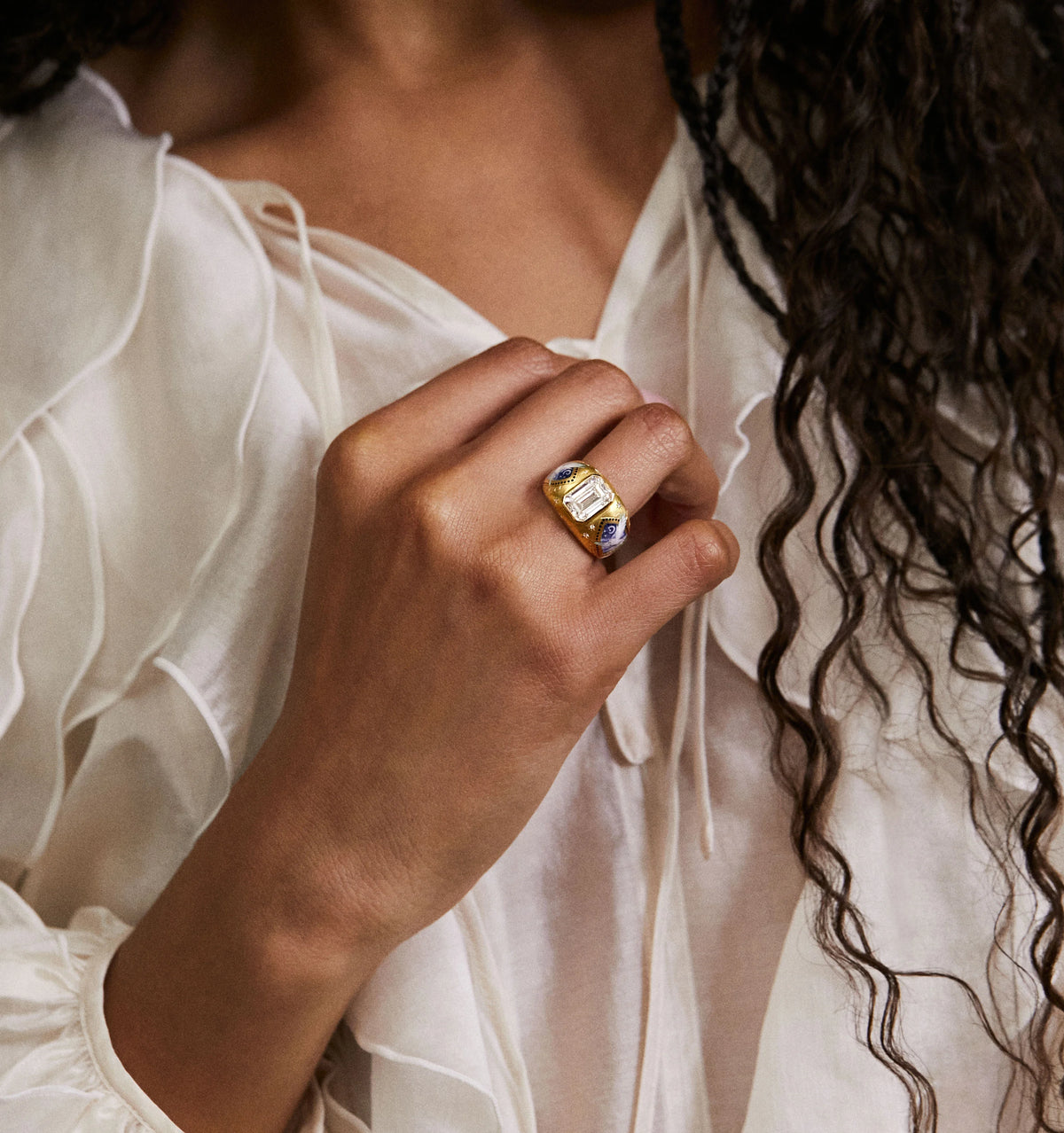 Woman wearing a gold ring featuring an emerald and sapphire design on her hand.