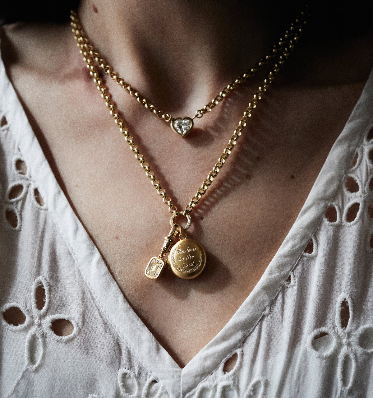 Woman wearing layered gold necklaces, one featuring a heart pendant and another with a round locket.