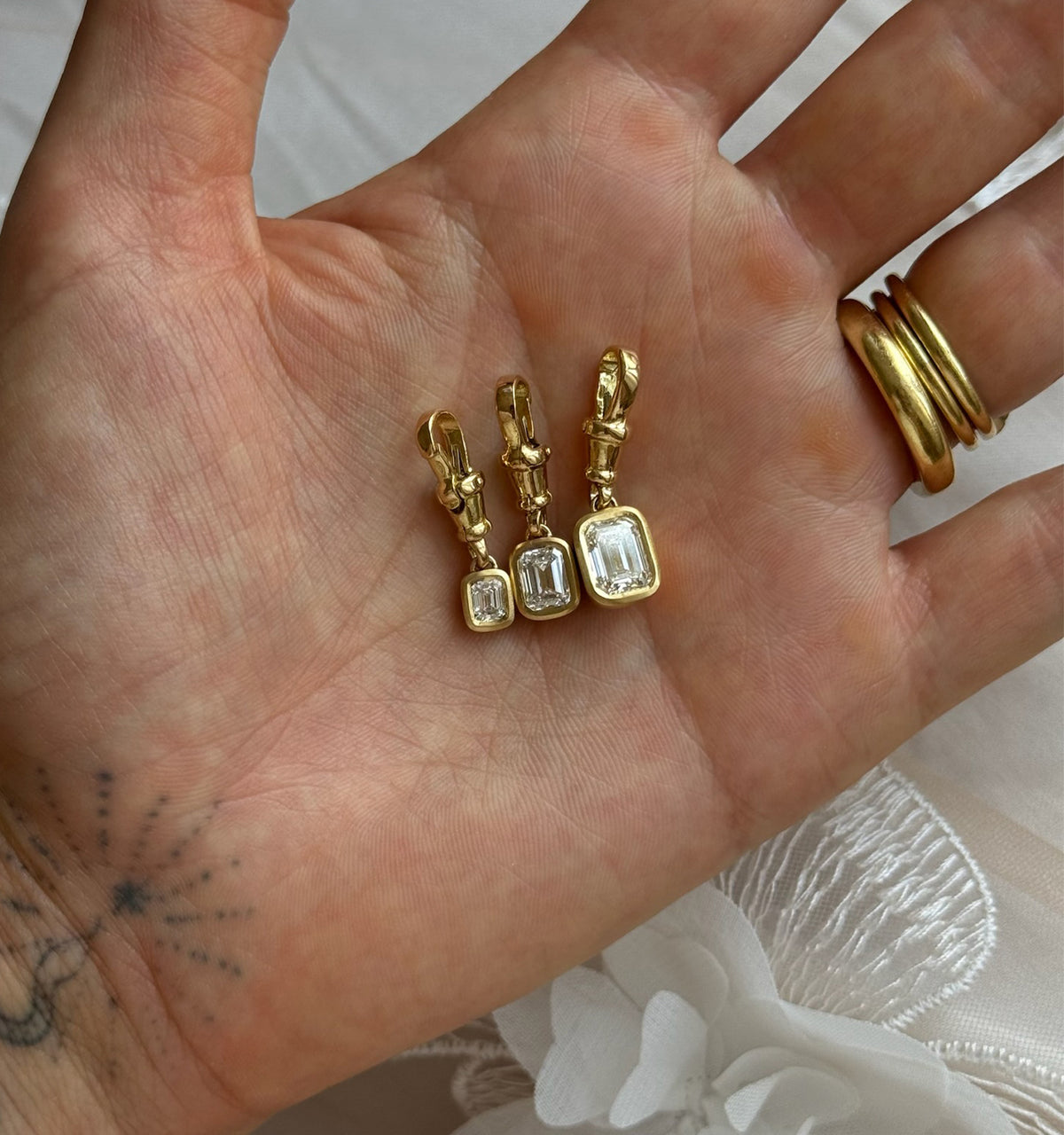 Gold drop earrings with rectangular diamonds, displayed in a hand.