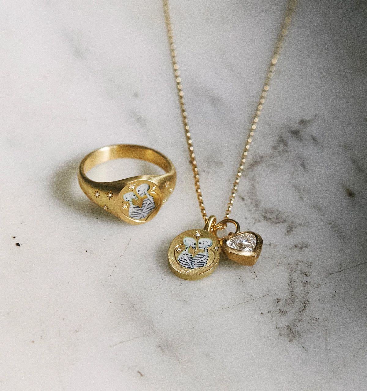 Gold ring with an engraved design and gold pendant necklace with enamel detailing and a heart charm.