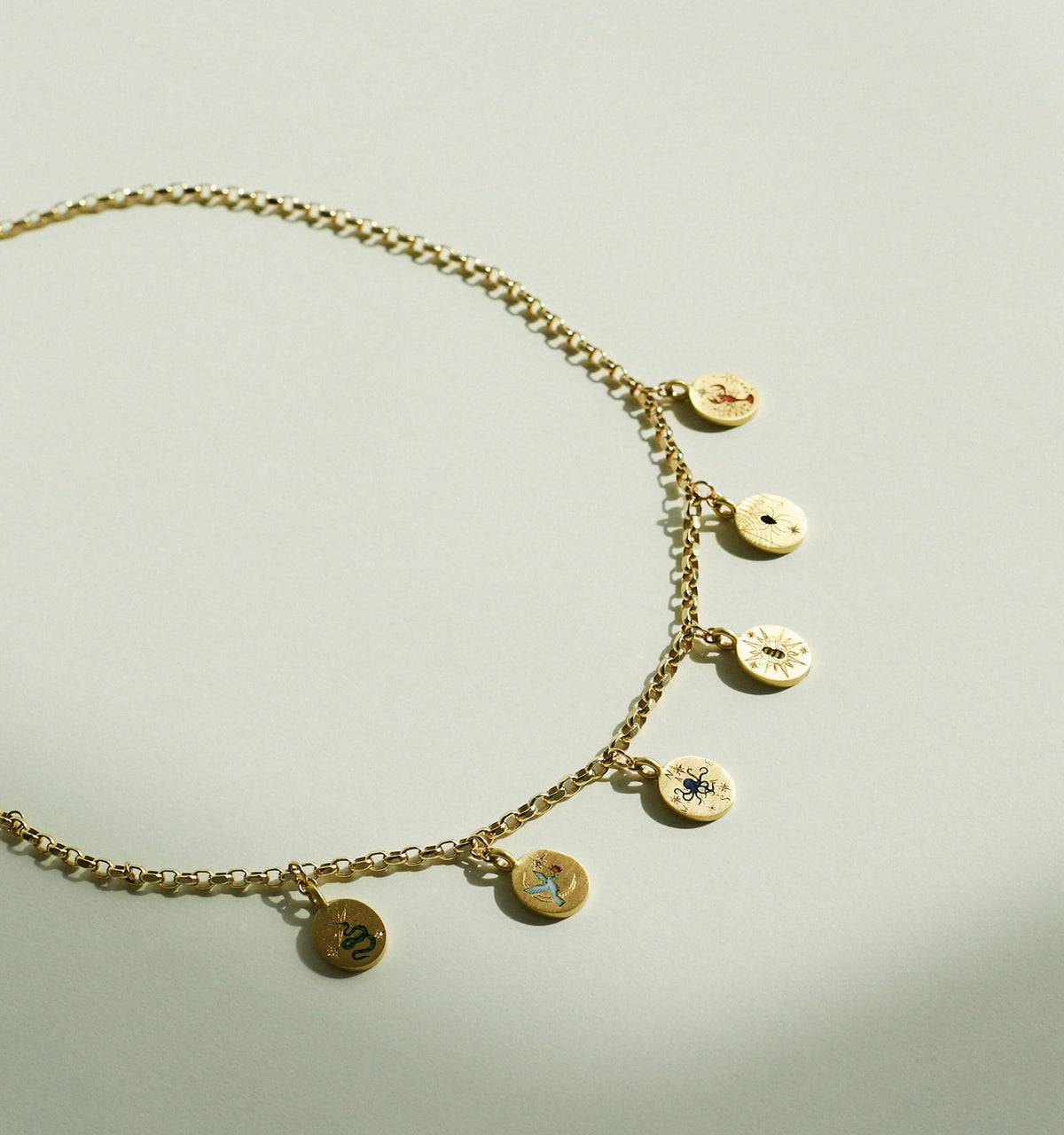 Gold chain necklace featuring engraved circular charms with various motifs.