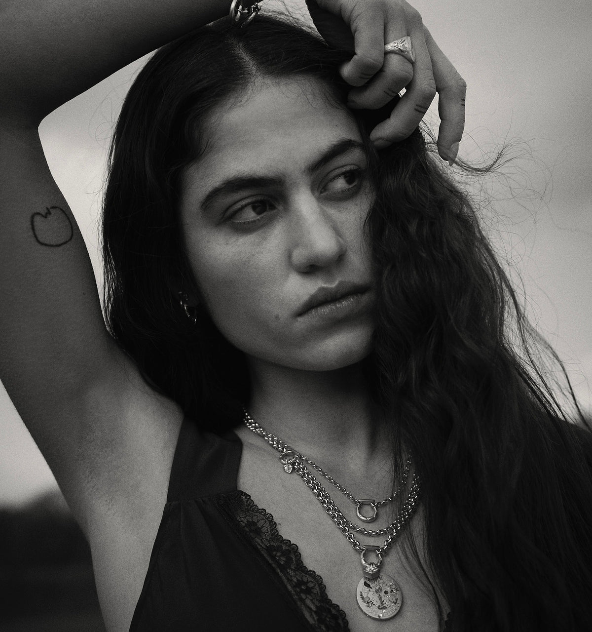 Woman wearing gold chains and a gold pendant, posing with long hair in a black lace outfit.