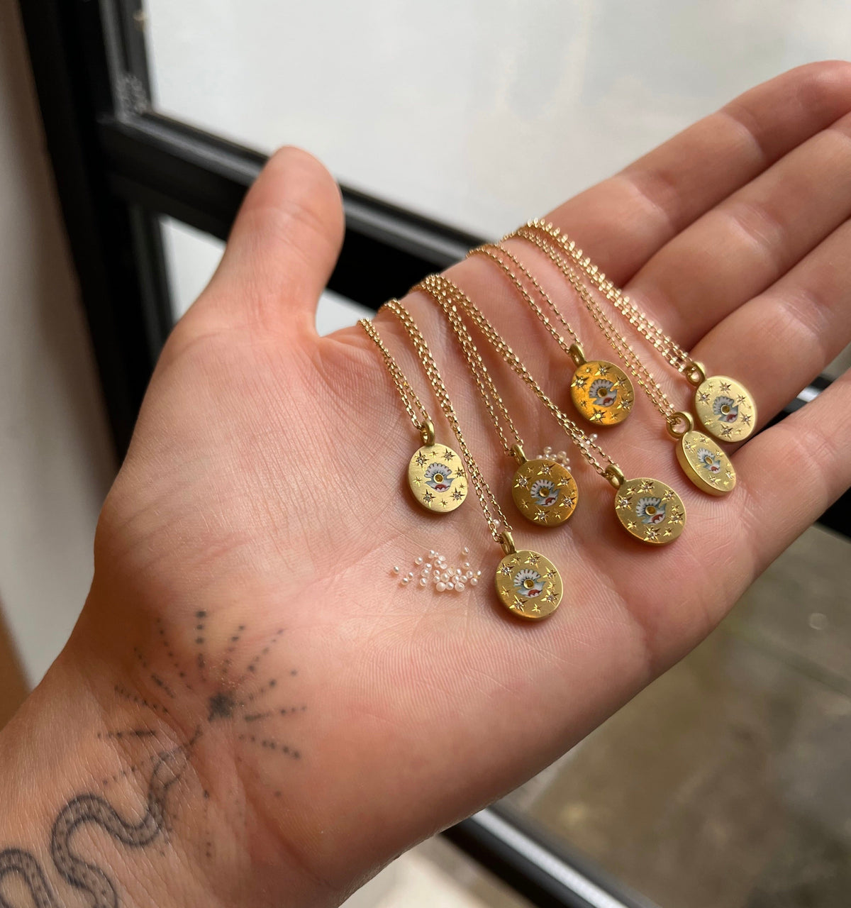 Gold necklaces with engraved sun and moon motifs displayed on a hand, with small beads nearby.