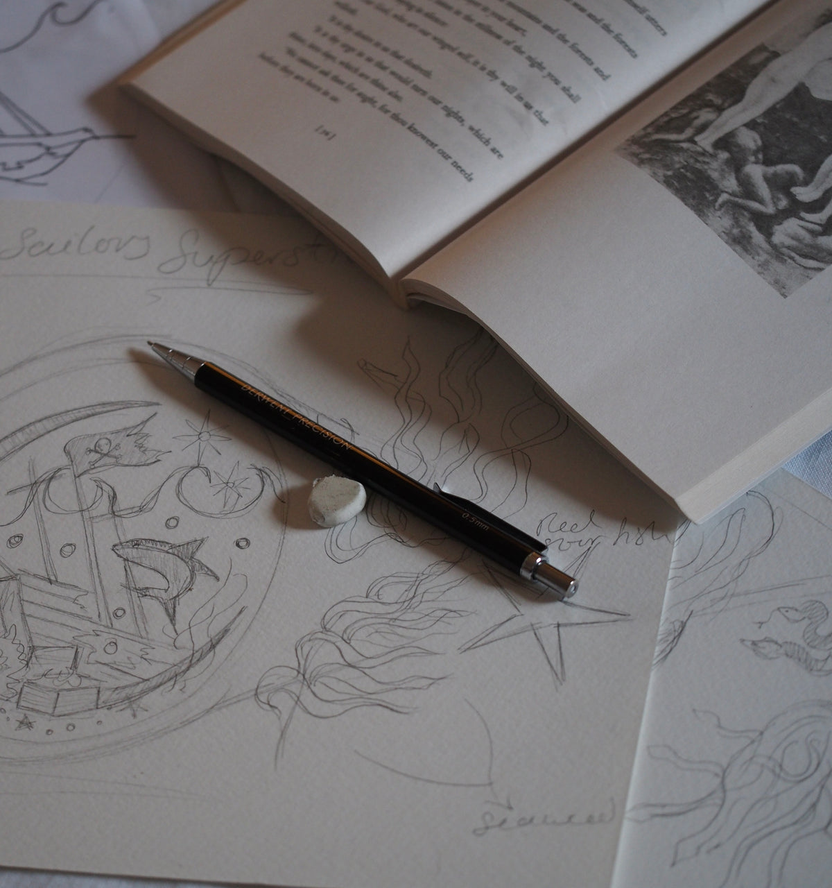 A sketchbook open to pages with detailed pencil drawings of nautical themes, accompanied by a pen and art supplies.